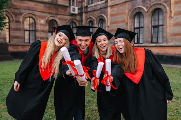 Successful graduates in academic gowns hold their diplomas look at the camera and smile for an outdoor photo