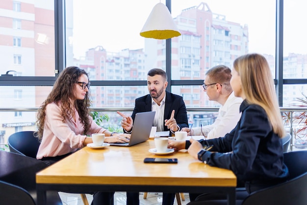 Successful handsome male mentor, director, businessman in a suit in an office with subordinates. Working day concept. Team meeting with the boss in the foreground