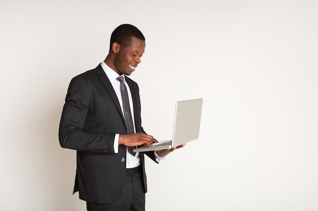 Successful, happy businessman in stylish official suit stands sideways, holding laptop at hands. Portrait. Copy space