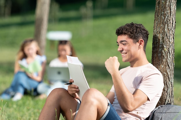 Successful hispanic student celebrating good results in the\
exam while sitting outdoors in a park