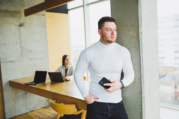 Successful male businessman in casual clothes smiling looking at phone standing in modern light office with phone working in modern company