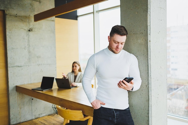 Successful male businessman in casual clothes smiling looking at phone standing in modern light office with phone working in modern company