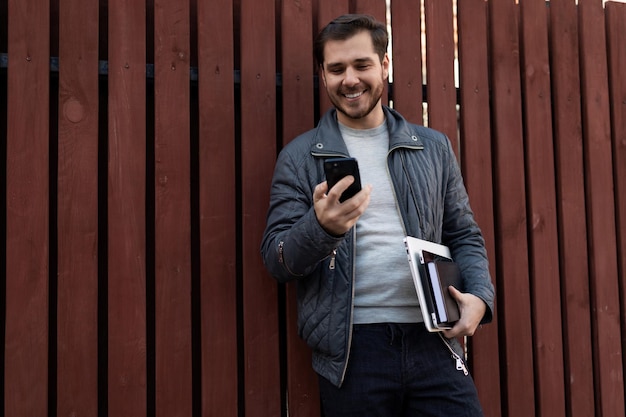 Successful male entrepreneur with a laptop in his hands looks at the screen of a mobile phone