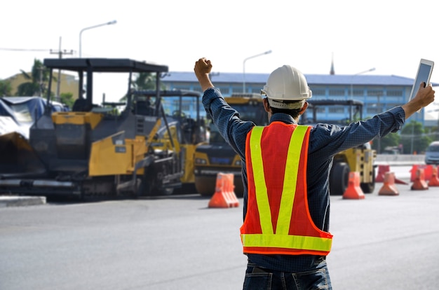 成功した男性の道路建設エンジニアは、完了中の建設プロジェクトに喜んで手を挙げました。