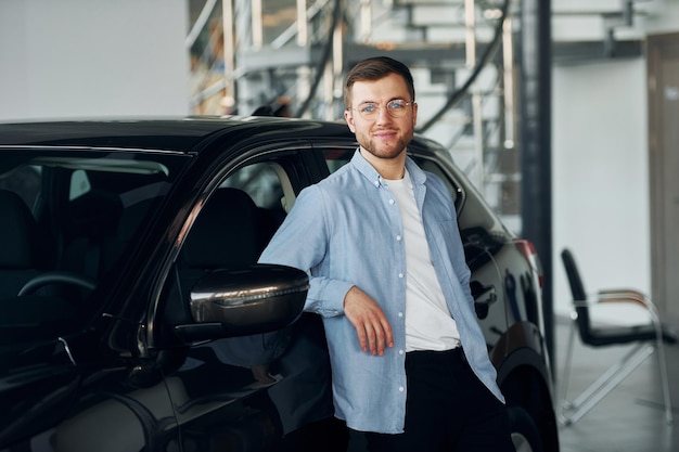 Successful man in glasses standing near brand new car indoors