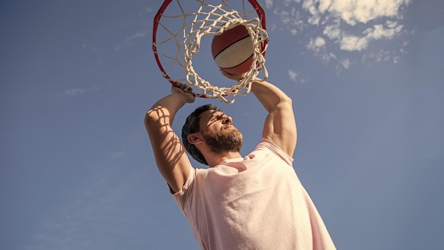 Successful man player throw basketball ball through basket on sky background summer