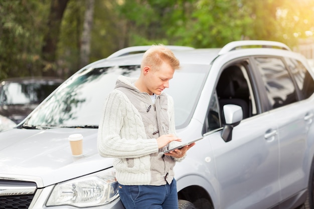 Successful man using a digital tablet pad while standing near his car outdoors.