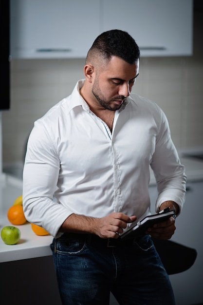 Successful man in a white shirt with a notebook in his hands stands near the table