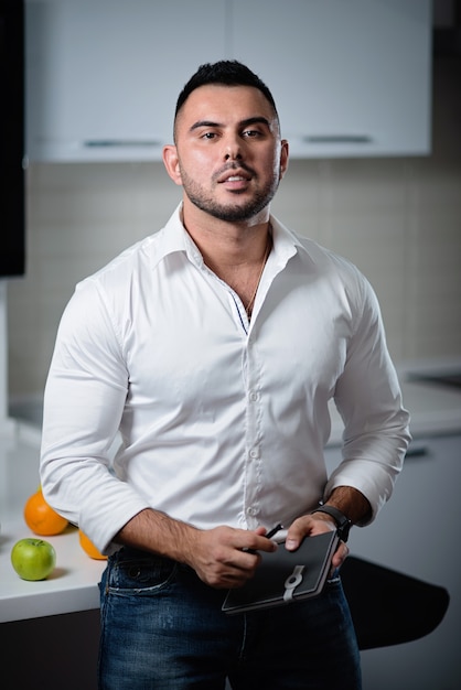 Successful man in a white shirt with a notebook in his hands stands near the table