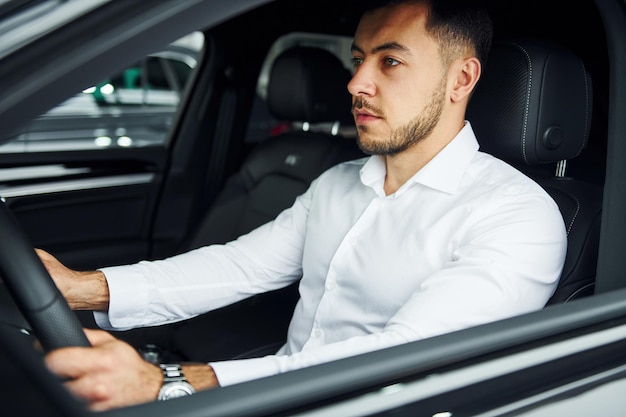 Successful man Young guy in white shirt is sitting inside of a modern new automobile