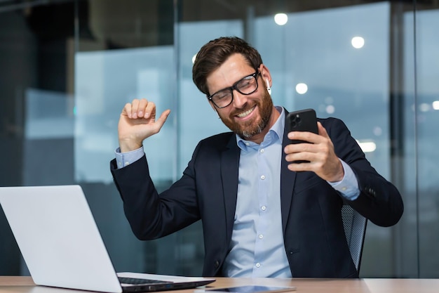 Photo successful mature businessman in office listening to music and dancing boss in glasses with phone