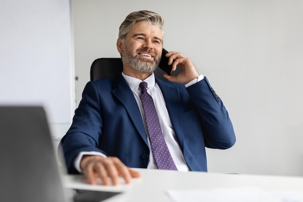 Successful mature businessman in suit talking on mobile phone at office