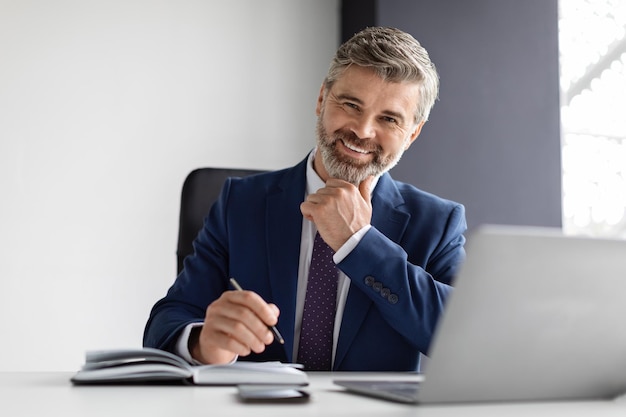 Successful mature businessman wearing suit sitting at desk with laptop in office