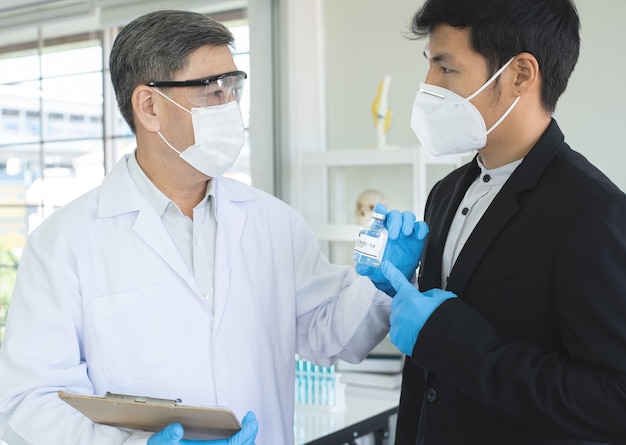 Foto ricercatore maschio maturo di successo o medico mostra il vaccino covid19 sull'invenzione di un nuovo vaccino a un uomo d'affari asiatico.