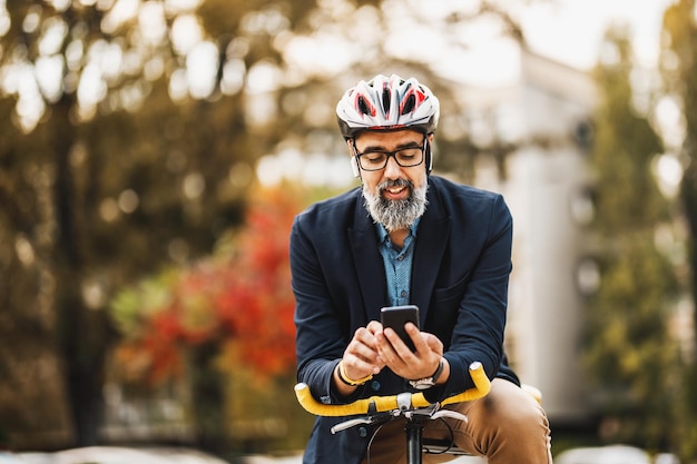 Successful middle-aged businessman using a smartphone on his way to work by bicycle  through the city.