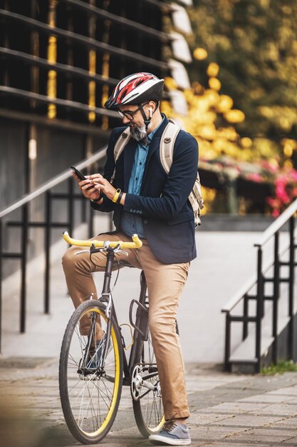 Successful middle-aged businessman using a smartphone on his way to work by bicycle  through the city.