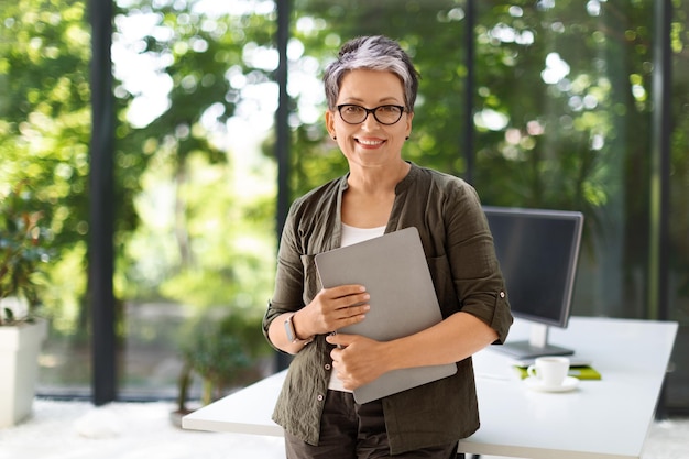 Successful middle aged lady posing with laptop at home office