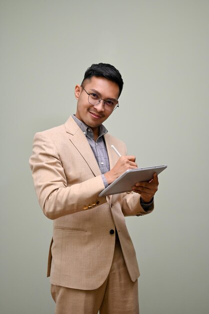 Successful millennial Asian businessman in formal business suit and glasses using his tablet