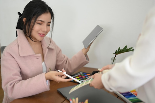 Successful millennial Asian female graphic designer manager working with her assistant at her desk