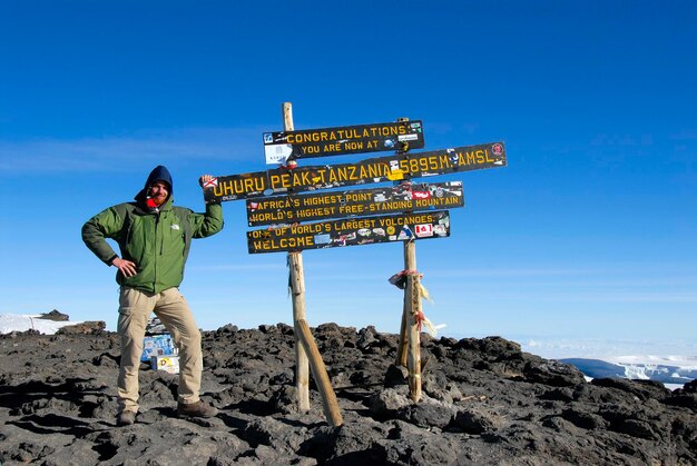 Successful mountaineer at the sign on the summit Uhuru Peak 5895 m crater rim Kilimanjaro Tanzania