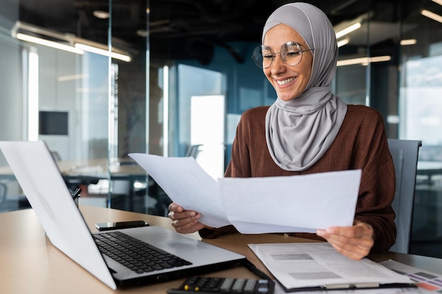 Successful muslim woman in hijab working inside office with documents joyful financial accountant