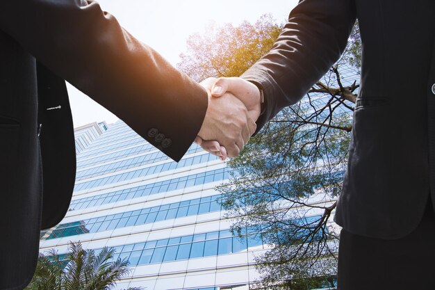 Photo successful negotiating business concept businessmen shaking hands after finishing meeting or setting goals and planning way to success in front of building