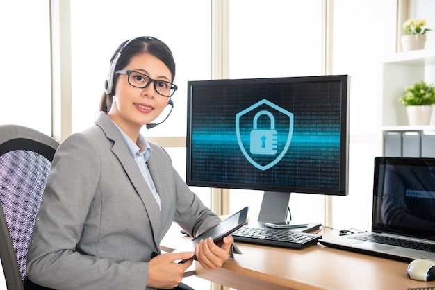 사이버 보안 회사에서 일하는 성공적인 사무실 여성, 디지털 태블릿을 들고 헤드셋을 착용하고 카메라를 대면하여 전문적으로 보입니다.