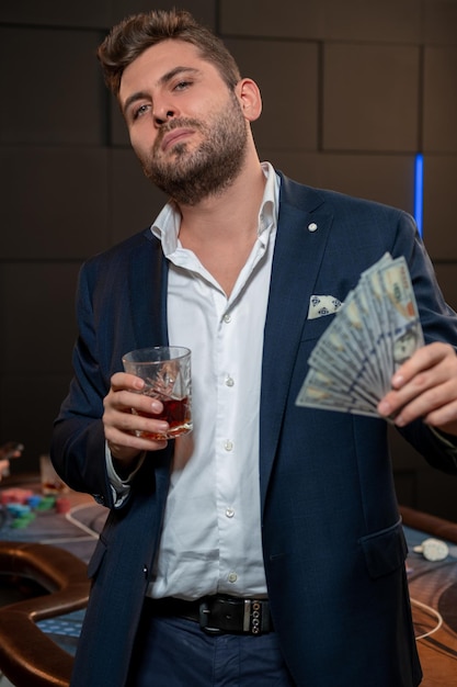Успешный игрок в покер с банкнотами и стаканом напитка в казино