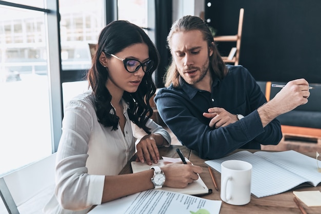 Successful professionals. Two young modern people in smart casual wear writing something down 