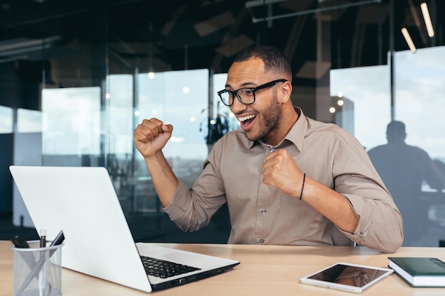 Successful programmer in office with laptop celebrating successful completion of software project