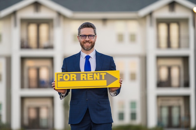 Successful real estate agent in suit with sign for rent Real estate broker front of rental new house Real estate home owner business man renting house new apartment in modern building