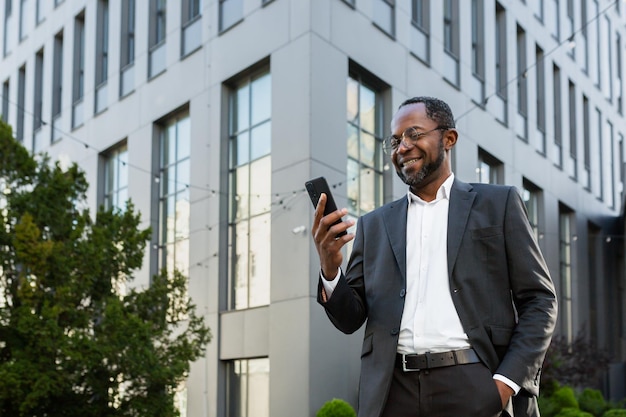 Successful and satisfied african american businessman using phone outside modern office building