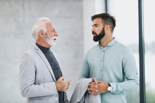 A successful senior businessman and his confiden young colleague walking and talking in a modern office.