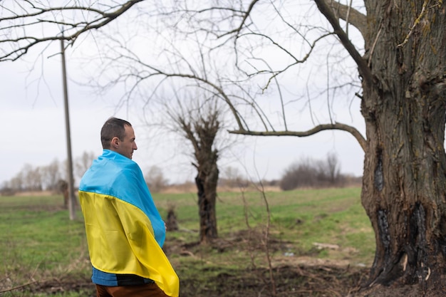 Successful silhouette man winner waving Ukrainian flag near a burnt tree