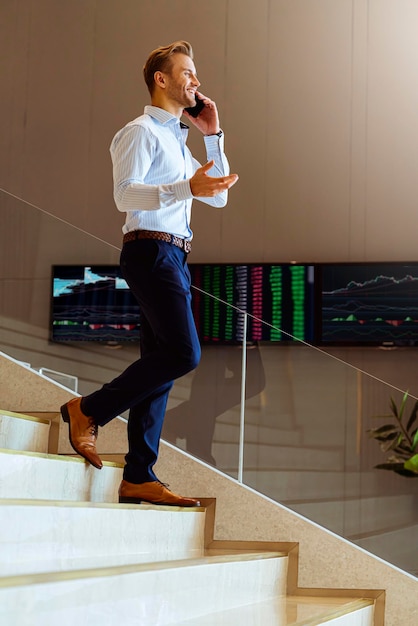 Successful smart caucasian businessman walking on stair make communication with smartphone communicate with happiness and enthusiastic modern office background