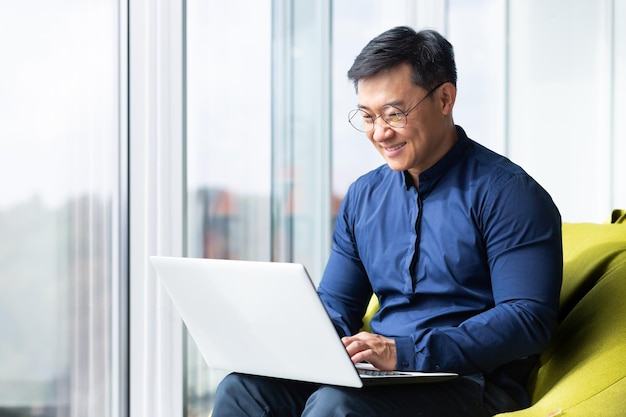 成功した笑顔のアジア人男性がノートパソコンの上級ビジネスマンと一緒にオフィス内でノートパソコンを操作