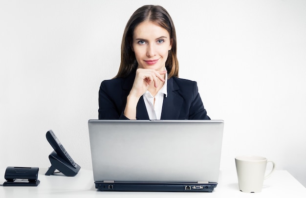 The successful smiling woman with the laptop sitting at  the office table indoors