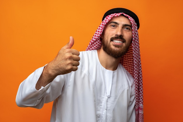 Successful smiling young arab man celebrating victory on orange background