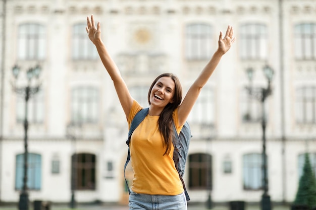 Успешная студентка радостная студентка колледжа поднимает руки и празднует успех на открытом воздухе