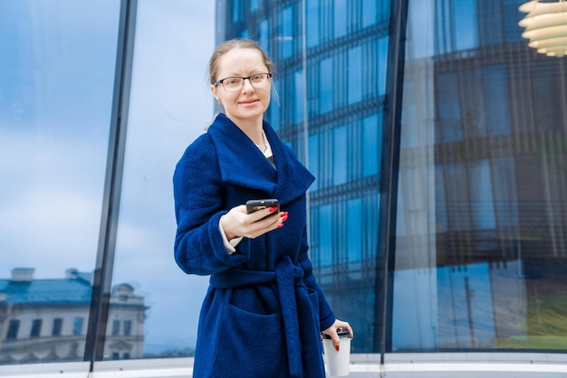 Successful woman in business clothes in blue coat walks down street near office