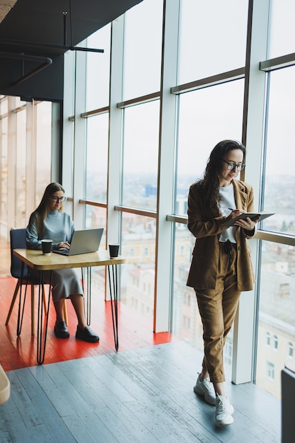 A successful woman in glasses works in the office on the background of colleagues Modern working day in the office Businesswoman makes notes in a notebook