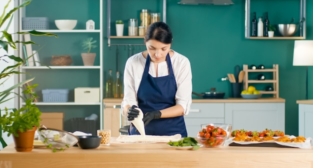 Successful woman pastry chef squeezes cream onto the cake using a culinary bag