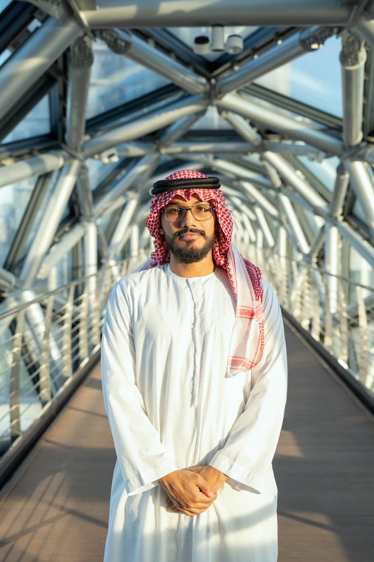 Photo successful young arab male delegate in national attire standing in front of camera against long aisle inside contemporary business center