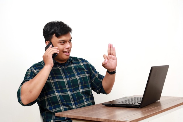 Successful young asian college student sitting while talking on the phone and using laptop on the desk with okay hand gesture