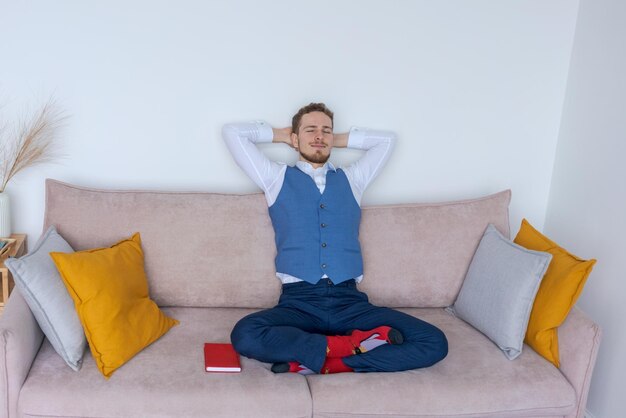 Successful young business man sits on sofa in lotus position in blue suit