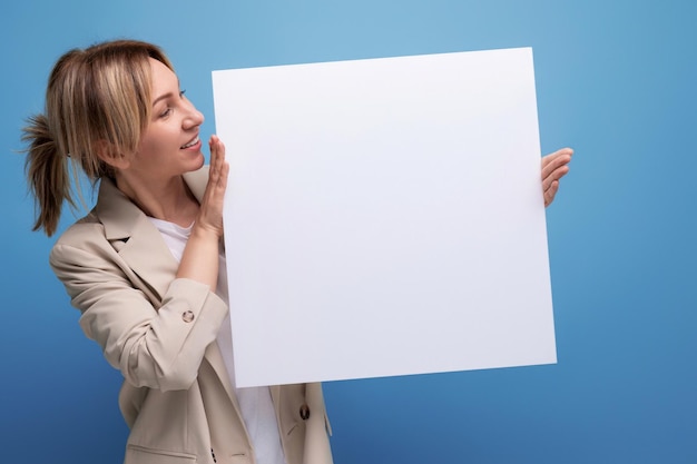 Successful young business woman holding blank placard for product presentation on studio background