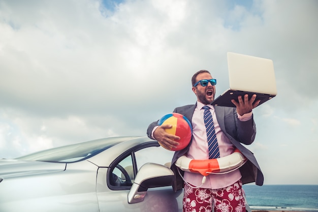 Successful young businessman on a beach Man standing near cabriolet classic car Summer vacations and travel concept