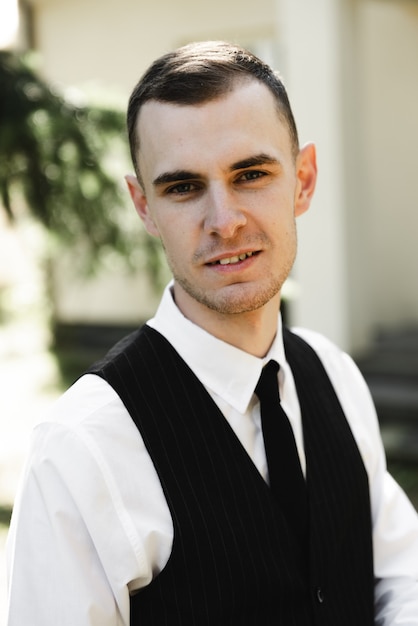 A successful young businessman dressed in formal clothes stands on the porch of his beautiful house. the groom's fees at home. portrait of a successful entrepreneur