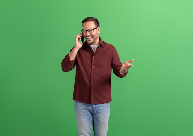 Successful young businessman sharing good news over smart phone while standing on green background