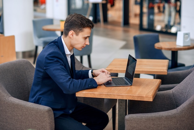 Riuscito giovane uomo d'affari che lavora al computer portatile in caffetteria